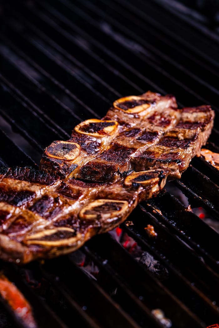 Close-up of sizzling beef short ribs perfectly grilled on a charcoal barbecue, showcasing the delicious meat texture.
