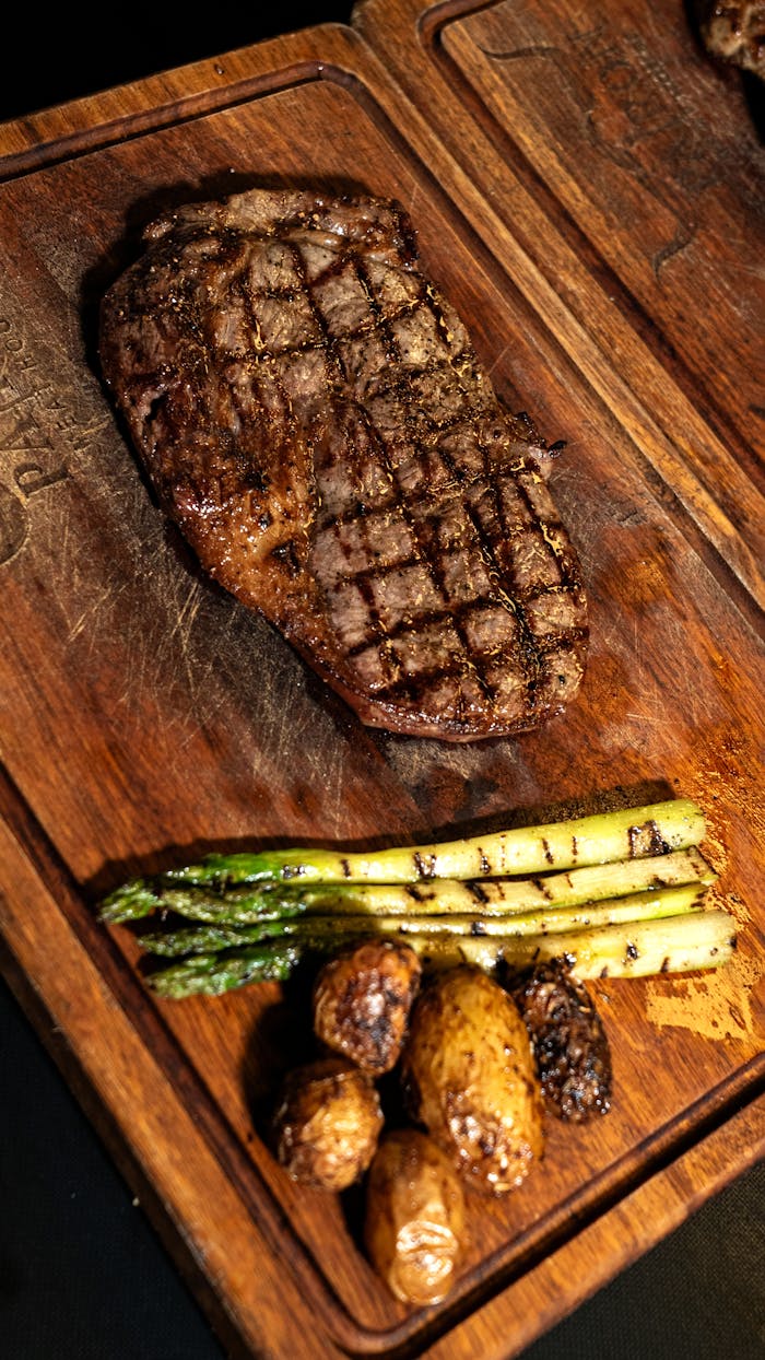 Juicy grilled steak served with asparagus and potatoes on a rustic wooden board, showcasing a hearty meal.